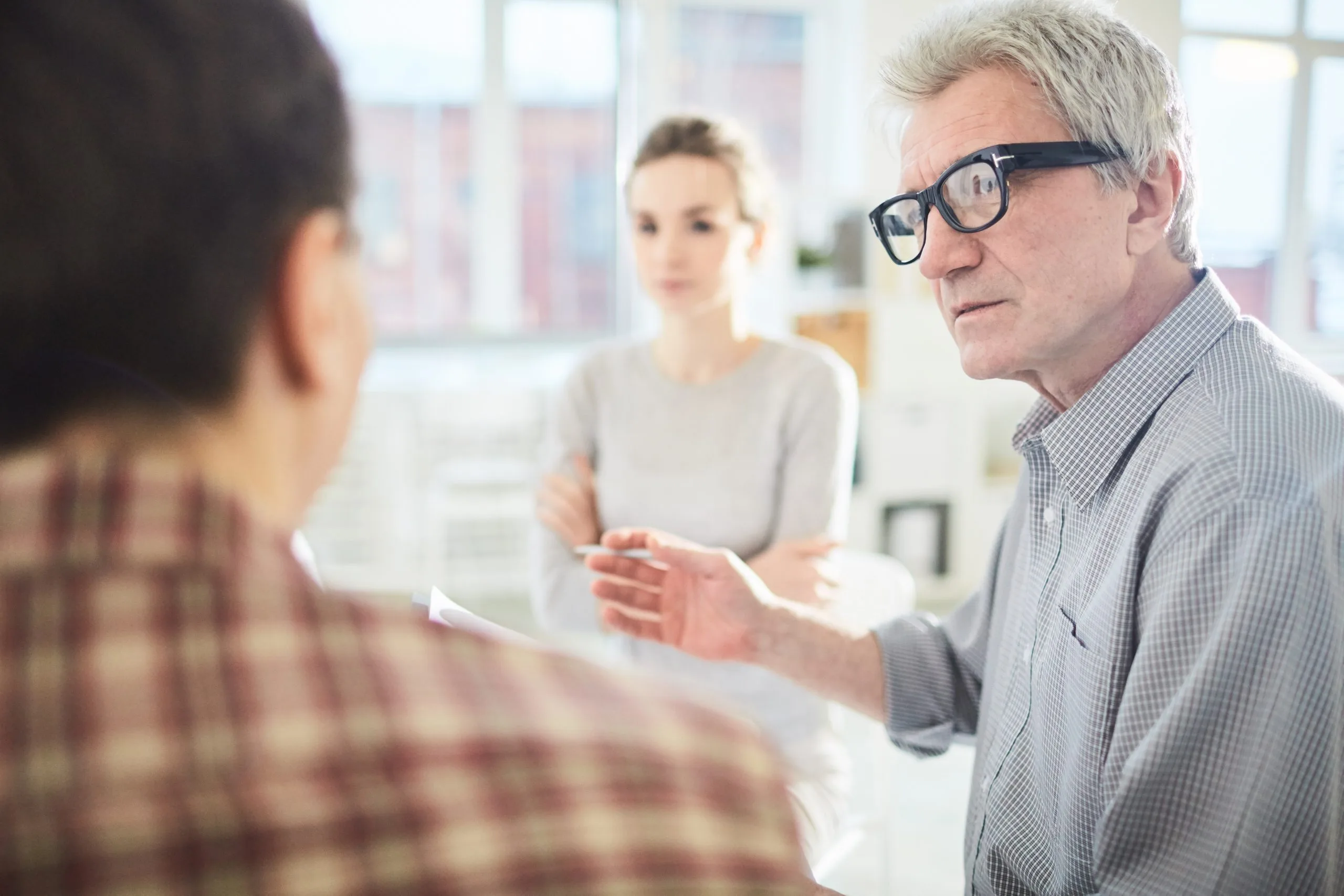 Mature leader of business team looking at one of employees while taking part in discussion of his ideas at start-up meeting